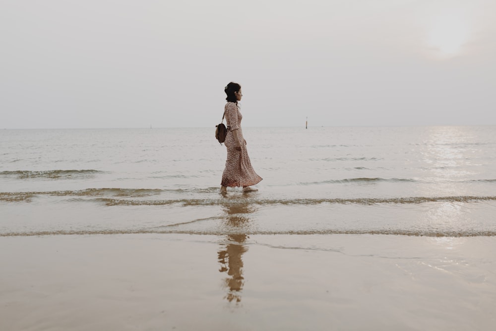 woman in pink dress walking on beach during daytime