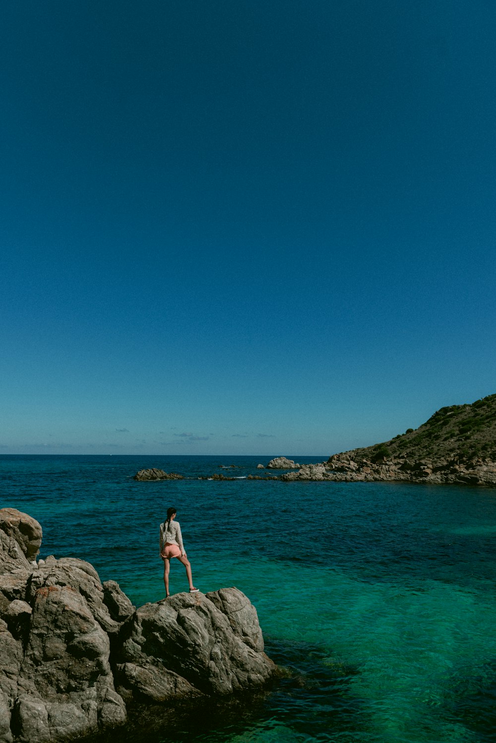 woman in white shirt standing on rock formation near sea during daytime