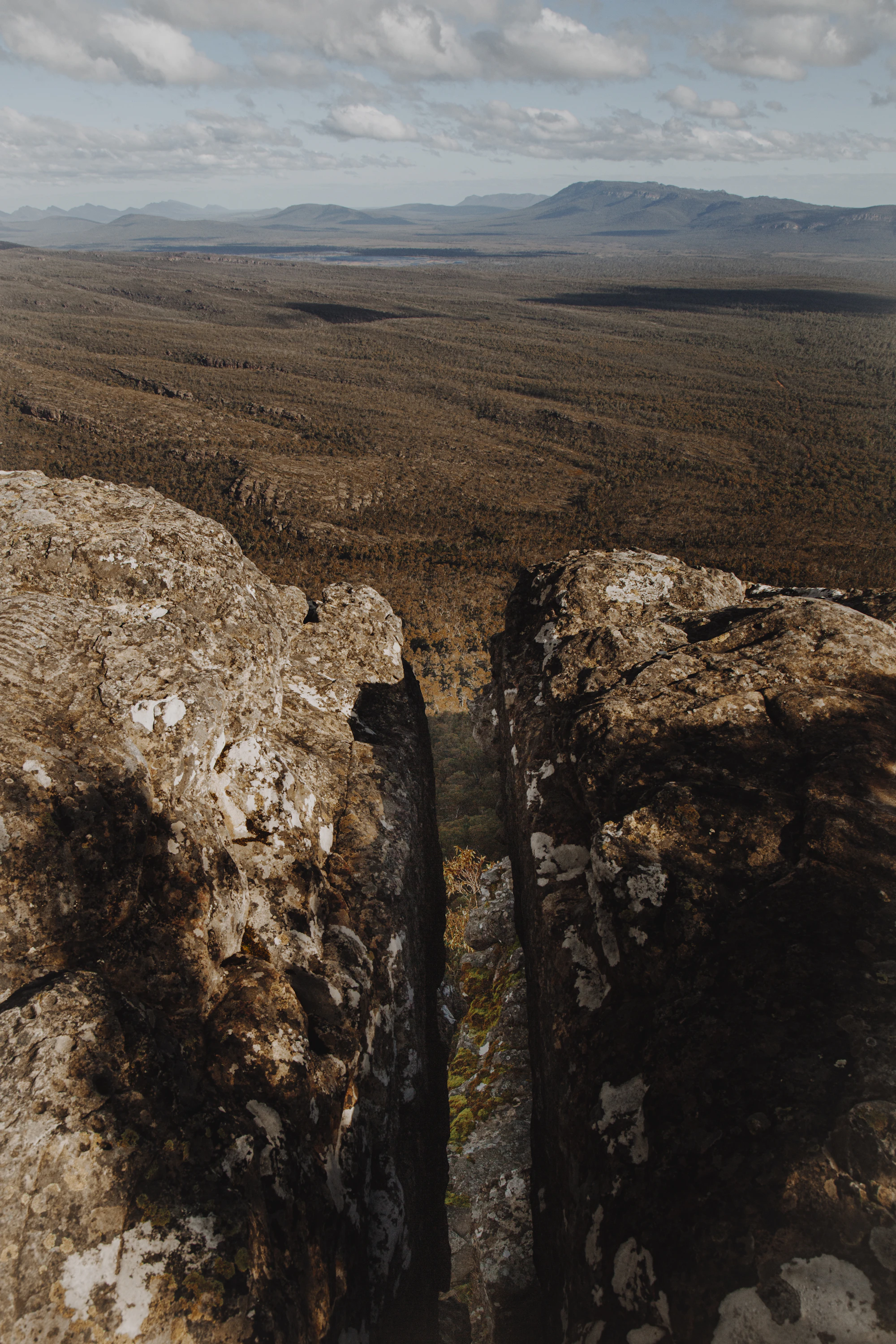 A rocky mountain viewpoint overlooking a wide wooded valley, with a deep narrow rock fissure in the foreground.