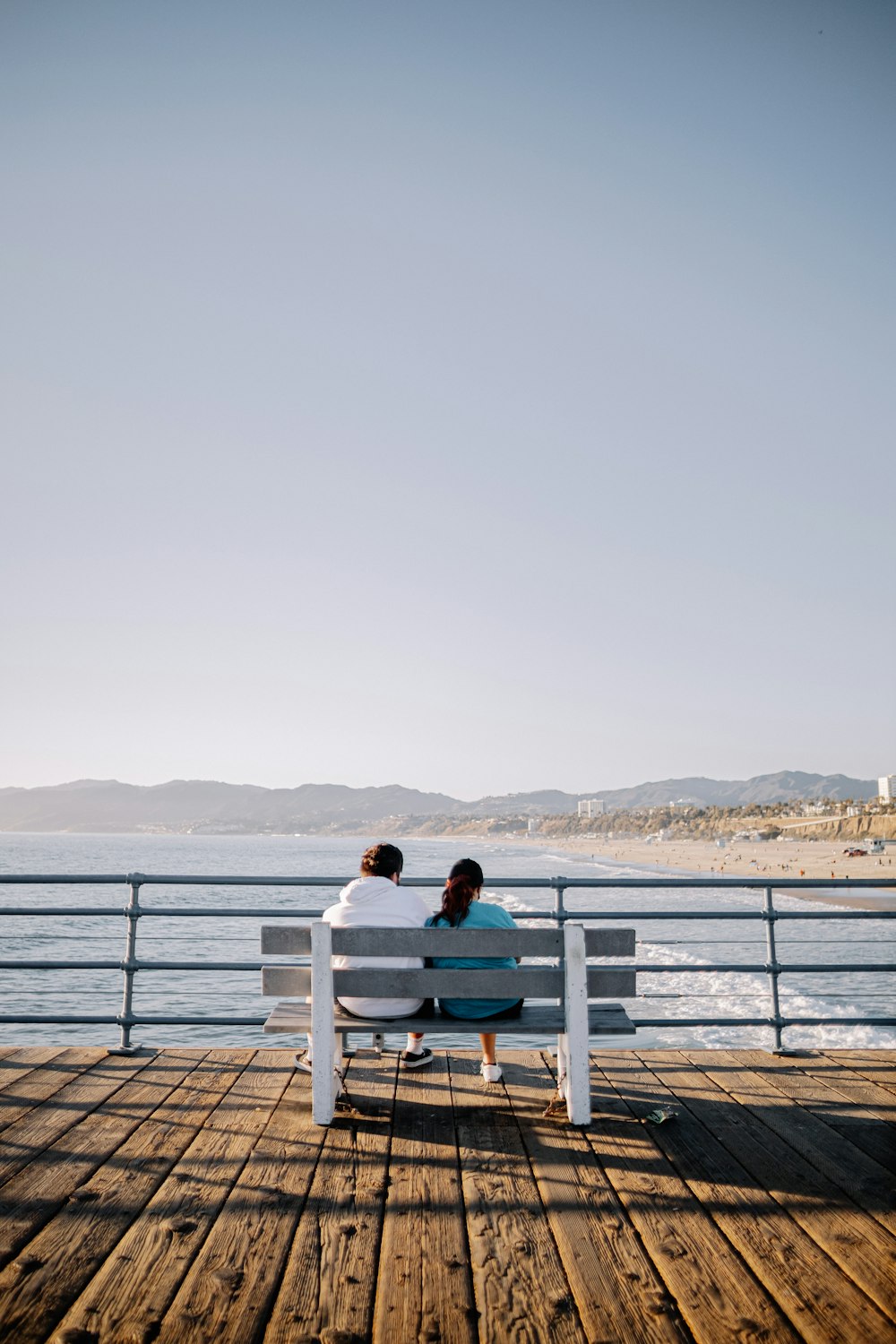 woman in teal shirt sitting on white wooden bench near body of water during daytime