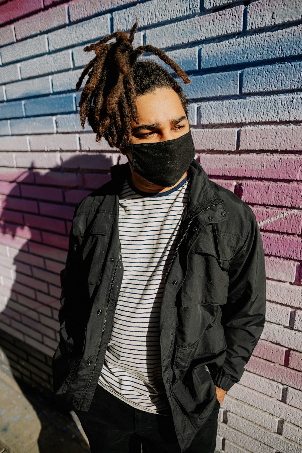 man in black leather jacket standing beside brick wall