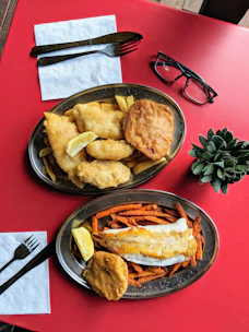 A rustic wooden table set with a steaming plate of classic pub fish and chips.