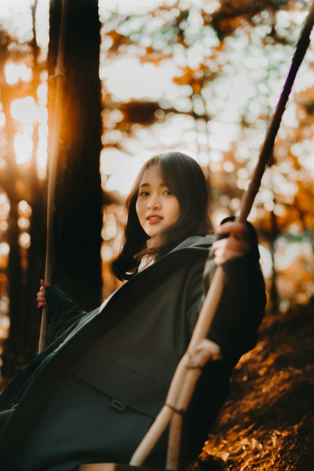 girl in black jacket holding on brown wooden swing during daytime