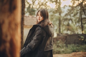 An outdoor shot of a woman in a modern tailored jacket, framed by soft natural light and muted urban background.