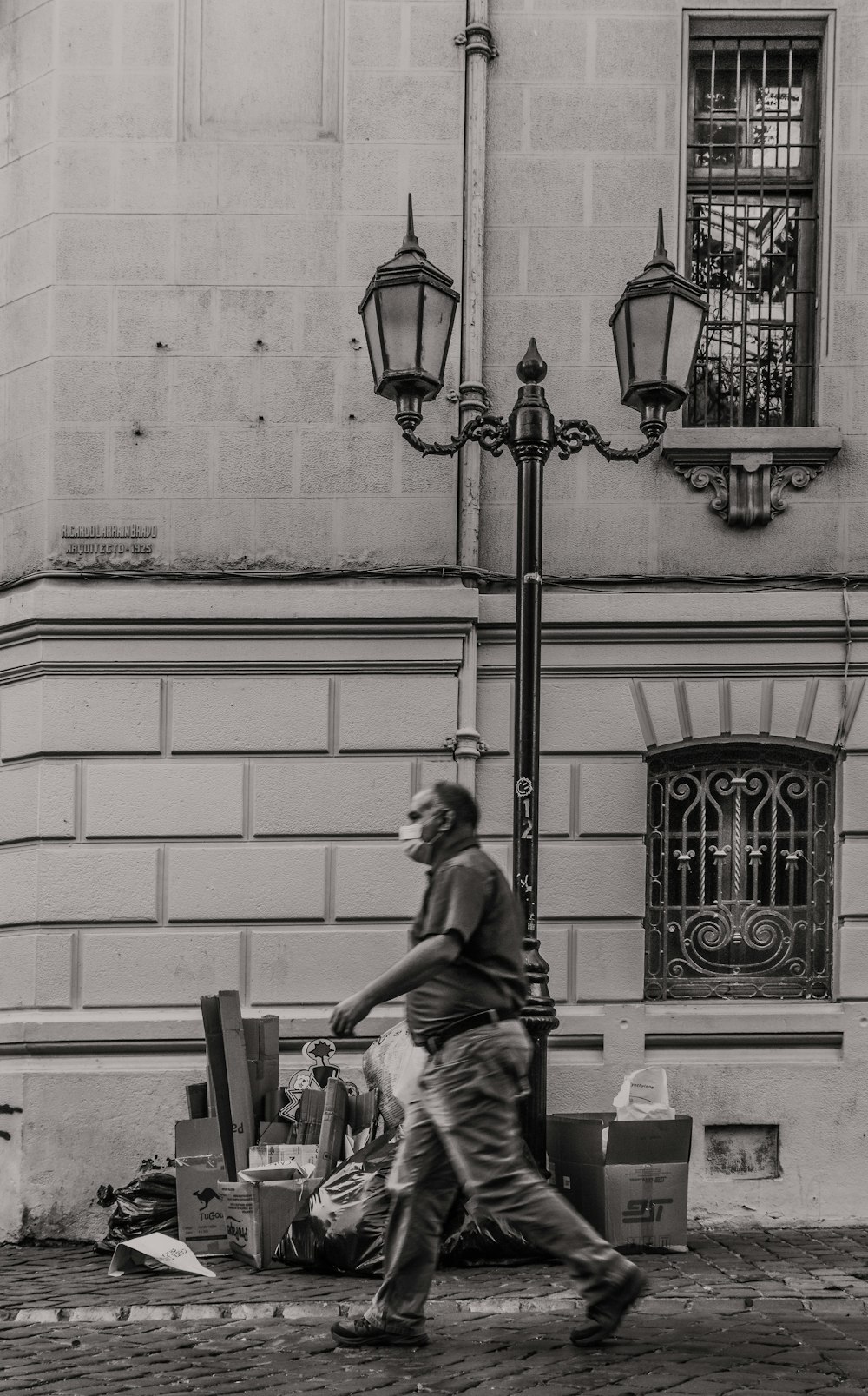grayscale photo of man sitting on bench near street light