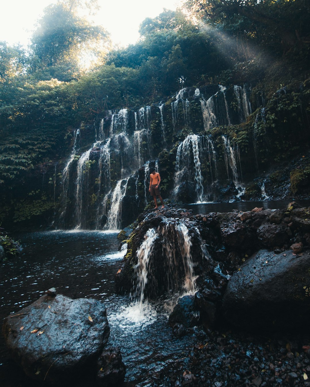 person in black jacket standing on rock formation in front of waterfalls during daytime