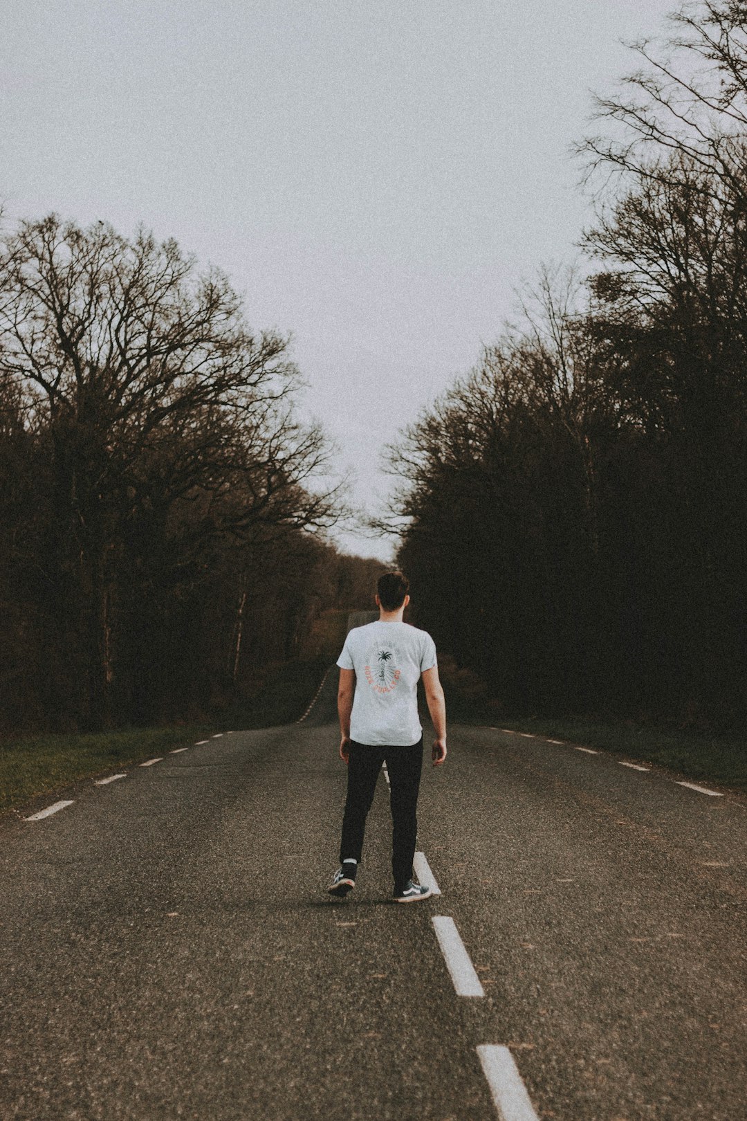 man in white t-shirt and black pants walking on gray asphalt road during daytime