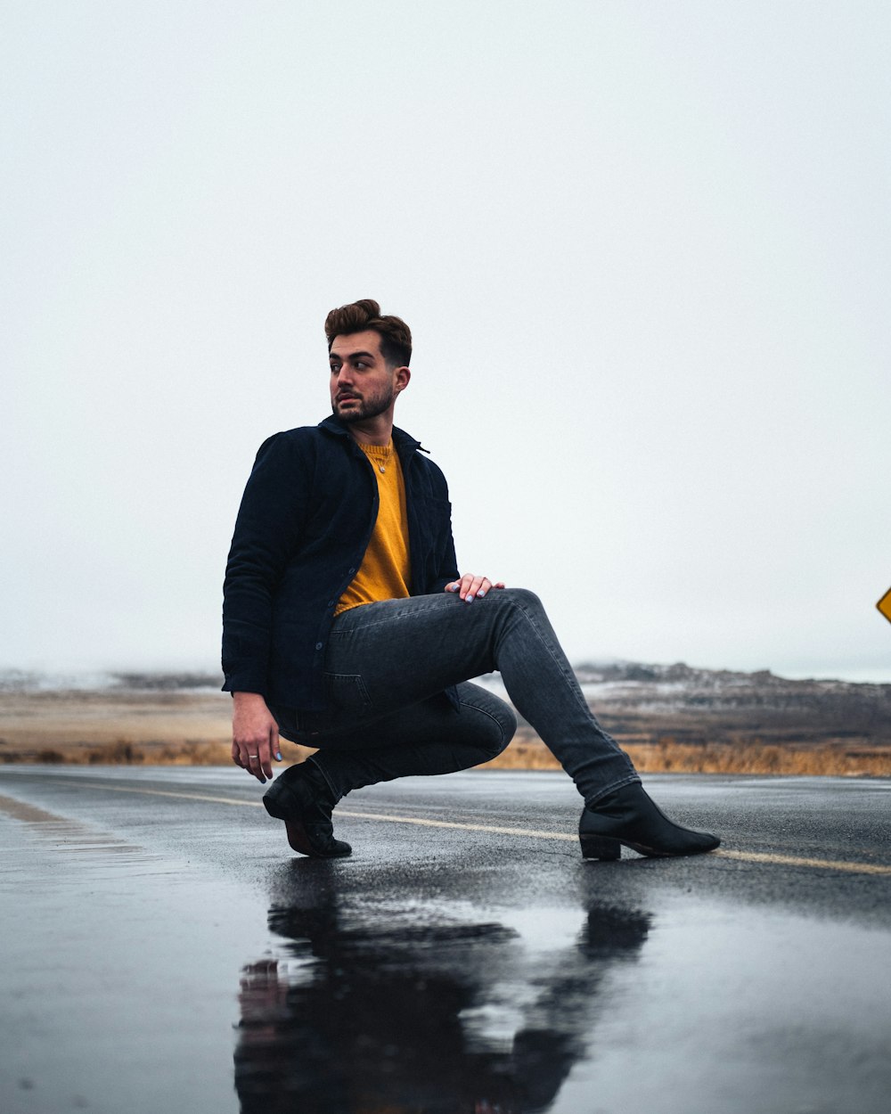 man in black jacket and blue denim jeans sitting on rock