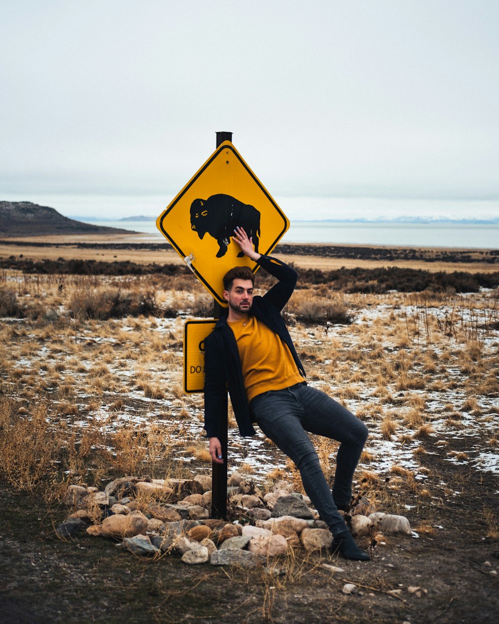 person in black jacket and blue denim jeans sitting on yellow and black road sign during
