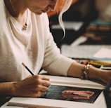 woman in white long sleeve shirt writing on white paper