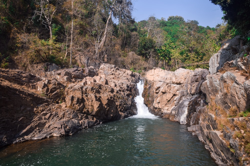 water falls between brown rocks and green trees during daytime