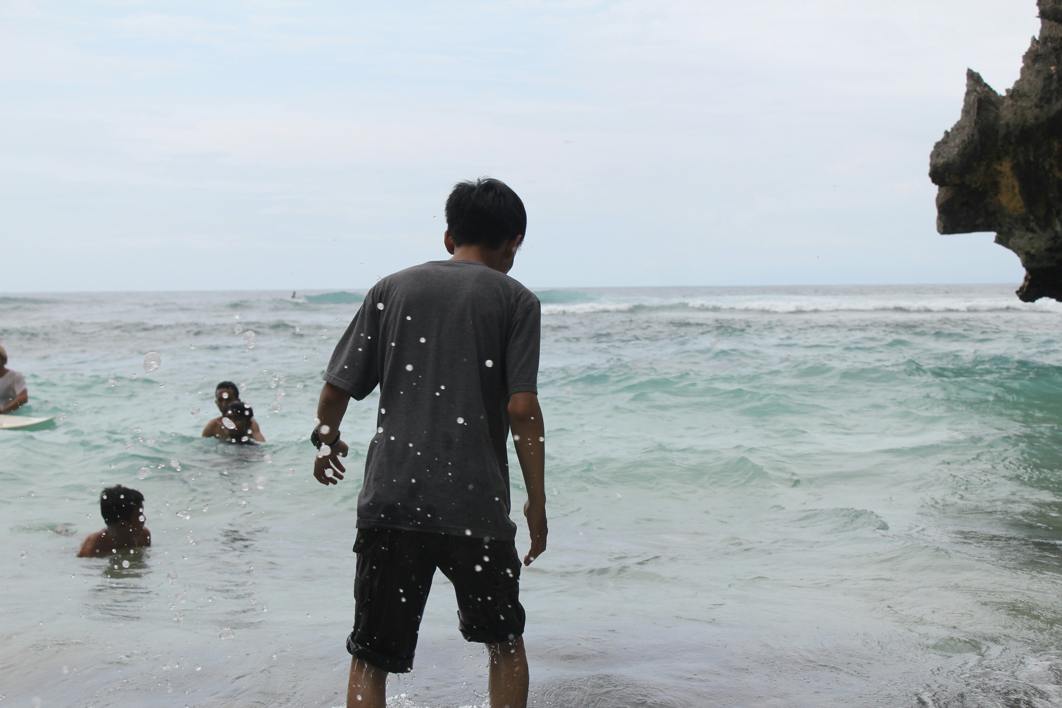 Pria berkaos abu-abu berdiri di pantai di siang hari