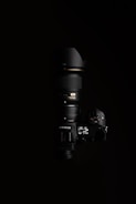 A high-end Nikon camera with a large lens, positioned against a black background. The lighting highlights the camera's buttons and display, showcasing the details of the camera body and the lens.
