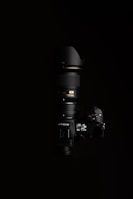 A high-end Nikon camera with a large lens, positioned against a black background. The lighting highlights the camera's buttons and display, showcasing the details of the camera body and the lens.