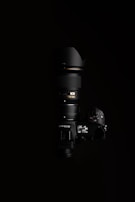 A high-end Nikon camera with a large lens, positioned against a black background. The lighting highlights the camera's buttons and display, showcasing the details of the camera body and the lens.