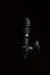 A high-end Nikon camera with a large lens, positioned against a black background. The lighting highlights the camera's buttons and display, showcasing the details of the camera body and the lens.