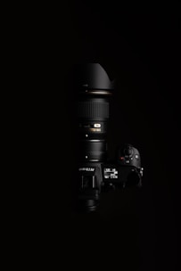 A high-end Nikon camera with a large lens, positioned against a black background. The lighting highlights the camera's buttons and display, showcasing the details of the camera body and the lens.