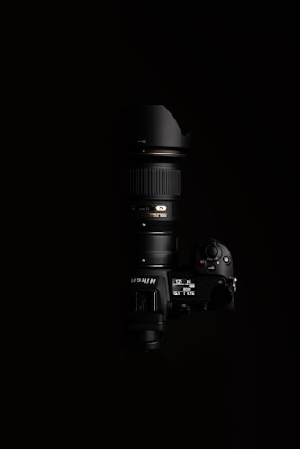 A high-end Nikon camera with a large lens, positioned against a black background. The lighting highlights the camera's buttons and display, showcasing the details of the camera body and the lens.