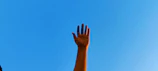 Hands raised in worship under a clear blue sky at an outdoor event.