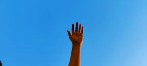 Hands raised in worship under a clear blue sky at an outdoor event.