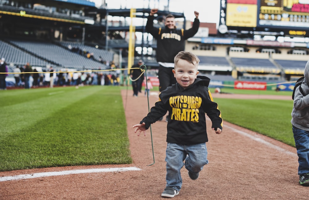 boy in black and yellow hoodie and blue denim jeans standing on brown field during daytime