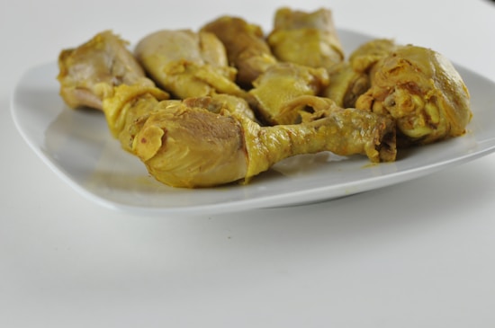 A plate with several pieces of cooked chicken drumsticks, seasoned and arranged on a white ceramic plate. The chicken is golden brown, suggesting it has been cooked with turmeric or curry. The simple presentation focuses on the food itself.