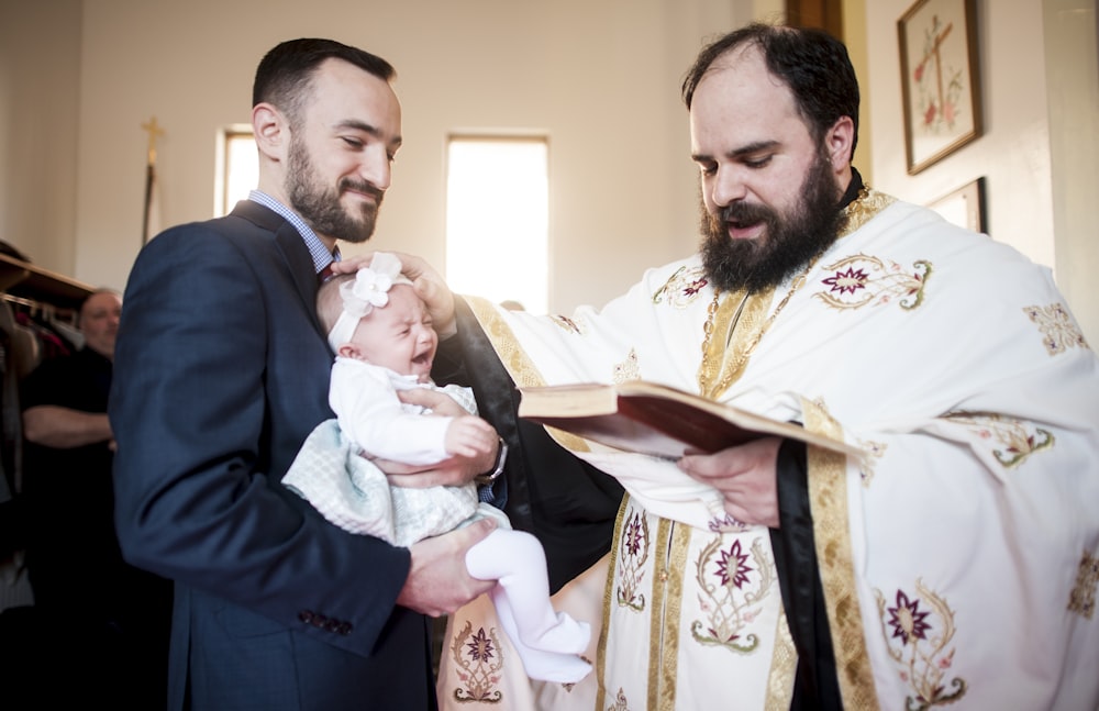 man in black suit holding baby in white dress