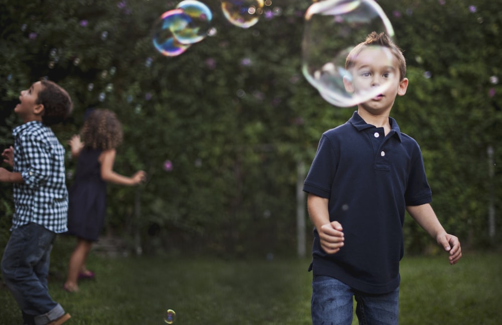 man in black polo shirt and blue denim jeans standing on green grass field with bubbles