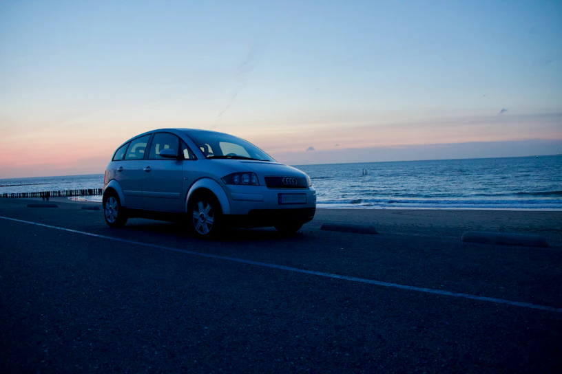 A sleek silver Volvo sedan parked on a scenic coastal road at sunset.