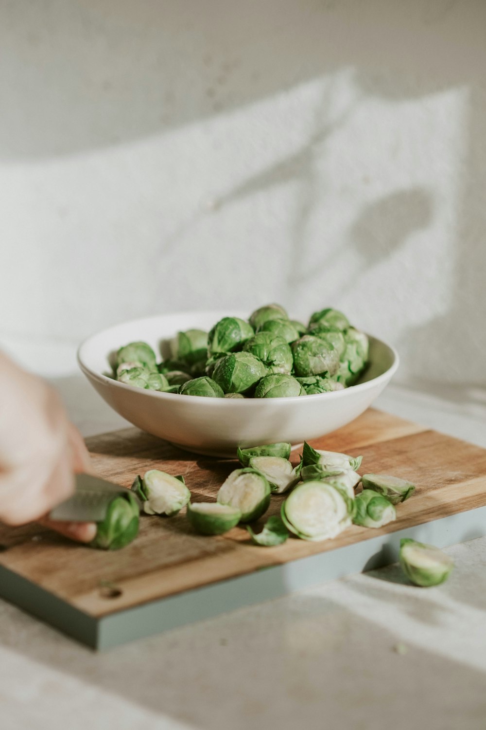 person slicing green vegetable on brown wooden chopping board