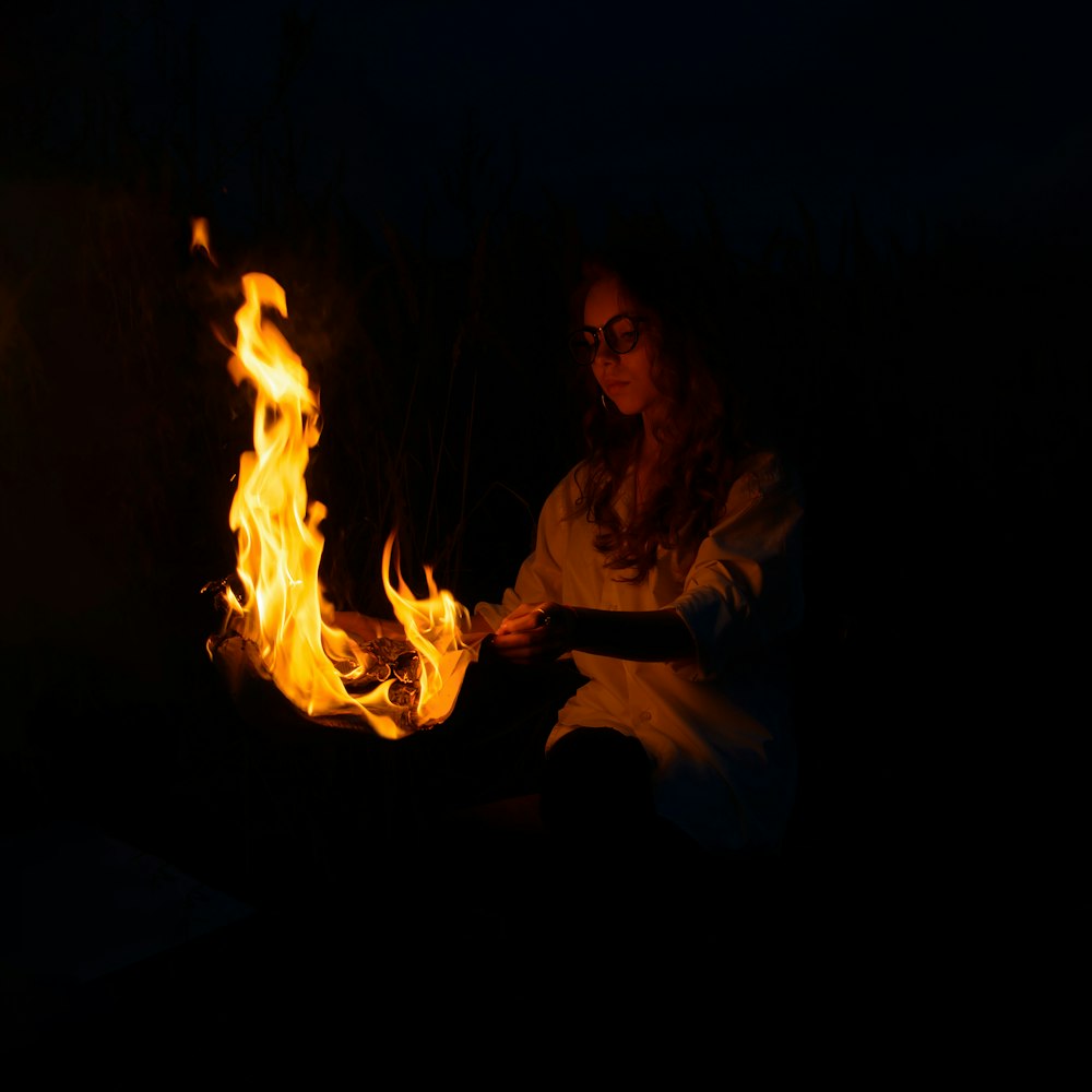 woman in white long sleeve shirt sitting on floor with fire