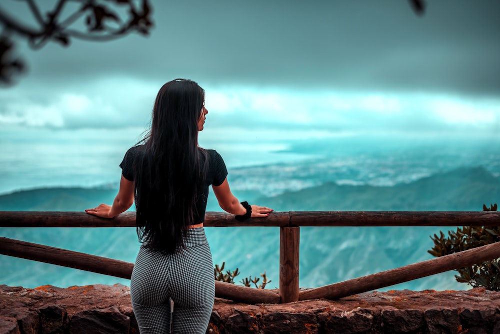 woman in black shirt and gray pants sitting on brown wooden railings during daytime