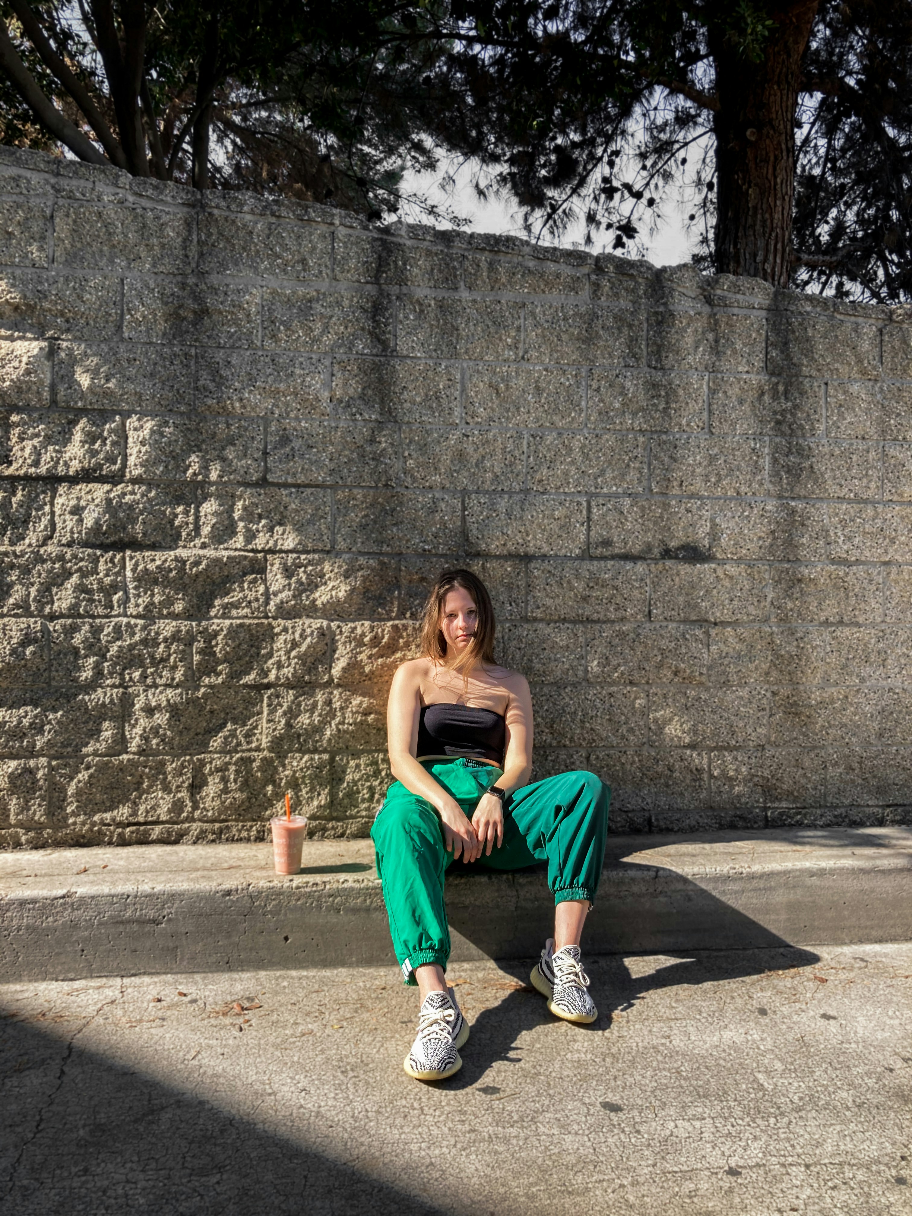 woman in orange tank top sitting on gray concrete wall during daytime