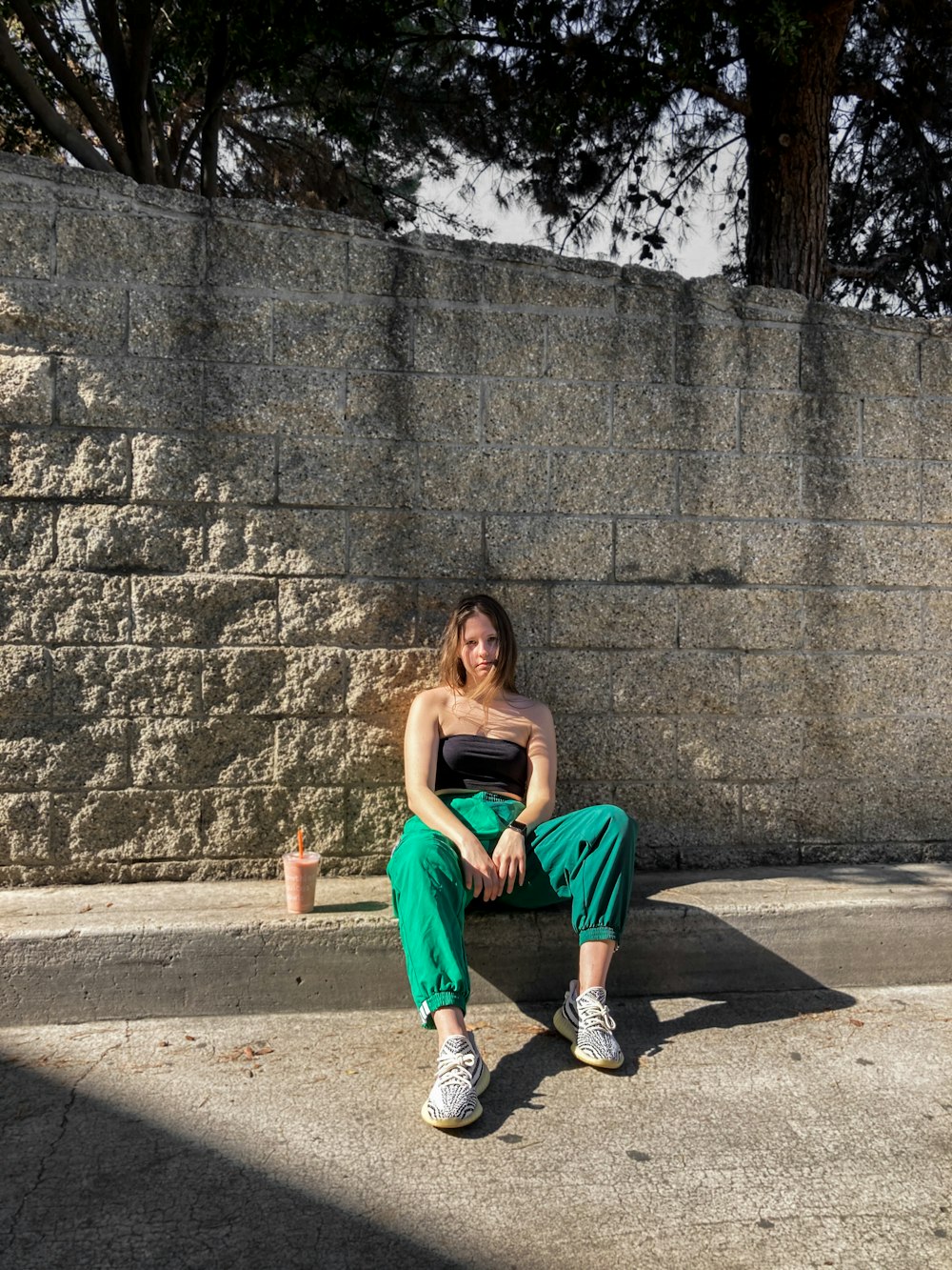 woman in orange tank top sitting on gray concrete wall during daytime