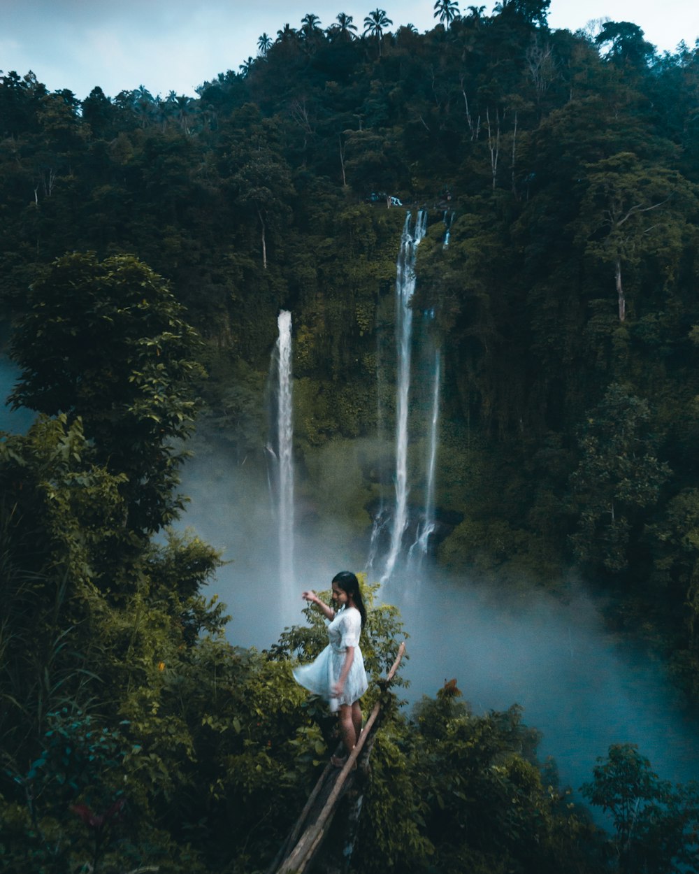 man in white shirt standing on brown rock near waterfalls during daytime