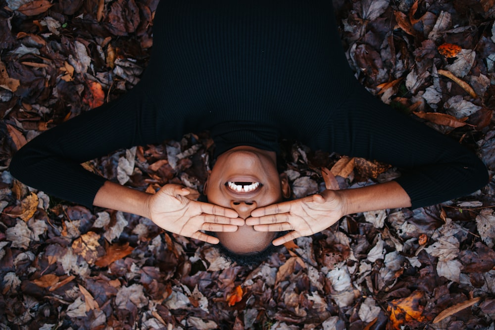 mulher na camisa preta de manga comprida deitada em folhas secas