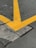 A cracked concrete surface intersected by large, bold yellow lines in a V shape, indicating a traffic or parking area. The pavement shows signs of wear with visible cracks and rough textures.