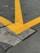 A cracked concrete surface intersected by large, bold yellow lines in a V shape, indicating a traffic or parking area. The pavement shows signs of wear with visible cracks and rough textures.