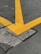 A cracked concrete surface intersected by large, bold yellow lines in a V shape, indicating a traffic or parking area. The pavement shows signs of wear with visible cracks and rough textures.