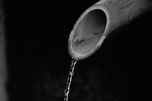 A close-up view of a partially visible pipe with water flowing out of its open end, set against a dark, indistinct background.