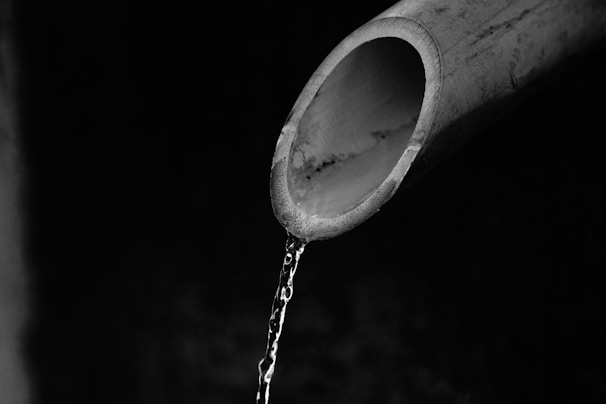 A close-up view of a partially visible pipe with water flowing out of its open end, set against a dark, indistinct background.