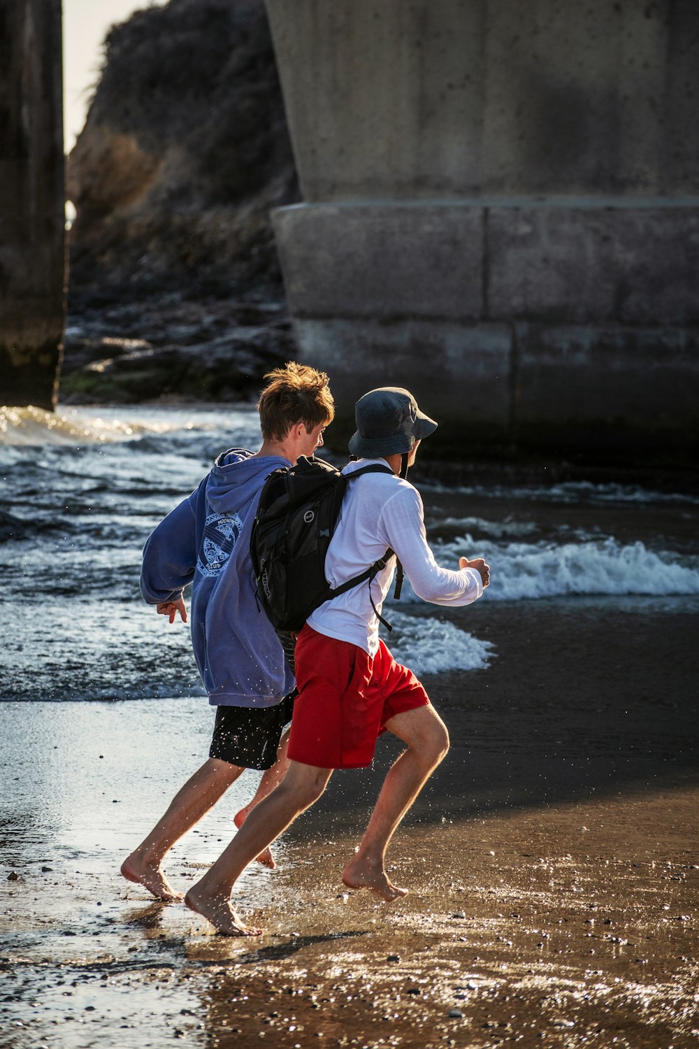 Hombre con chaqueta azul y pantalones cortos rojos caminando en la playa durante el día