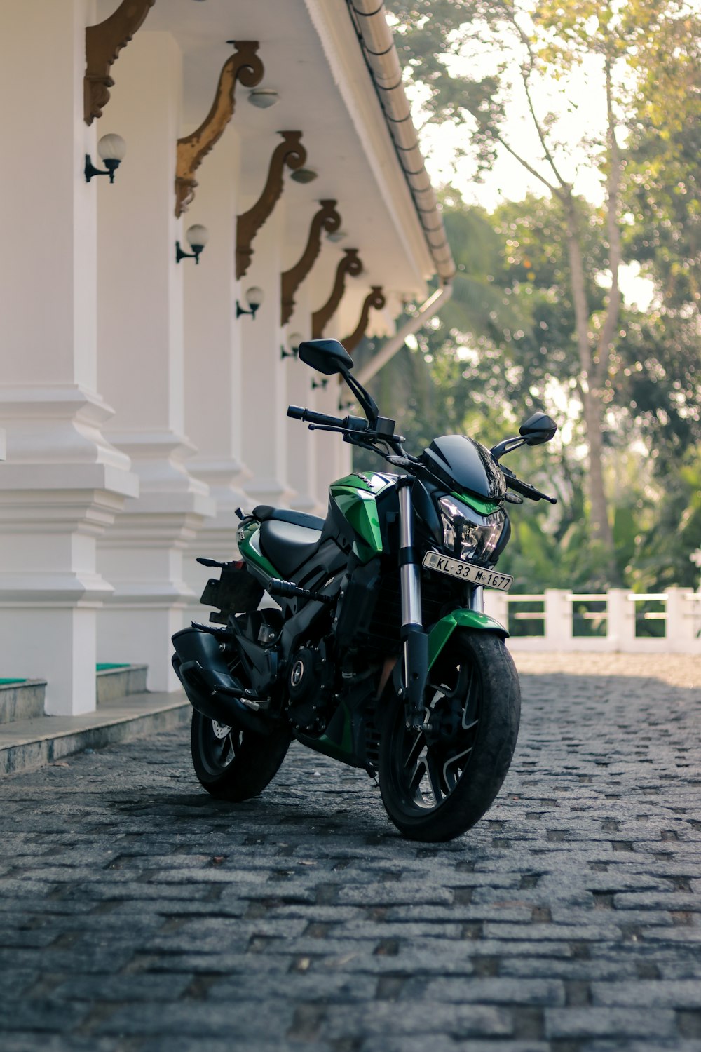black and green naked motorcycle parked beside white building during daytime