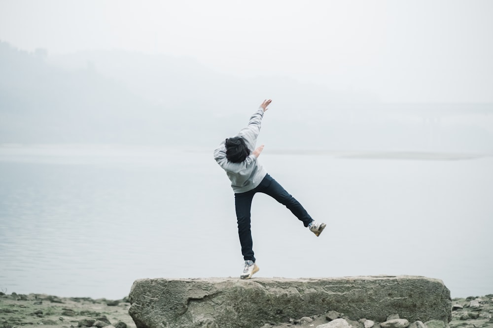 man in gray hoodie and blue denim jeans jumping on brown rock