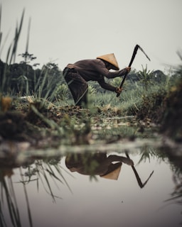 man in brown long sleeve shirt and black pants sitting on grass field while reading book
