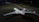 Two private jets are parked on a dimly lit runway at night, with one jet in the foreground and another in the background. The scene is illuminated by artificial light, reflecting off the sleek surfaces of the aircraft. The ground is marked with various lines and labels typical of an airport taxiway.