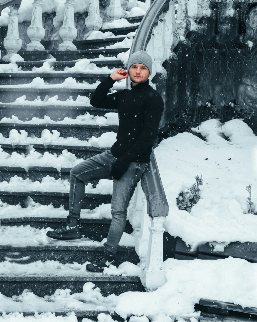 man in black jacket and blue denim jeans sitting on gray concrete staircase