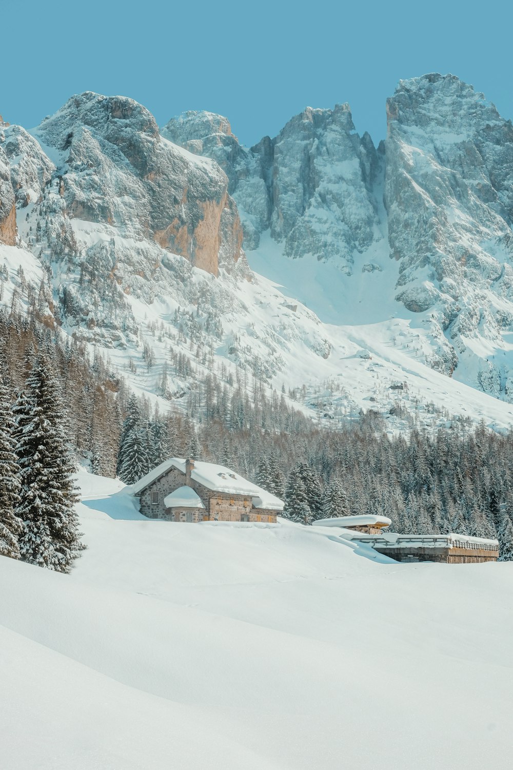 Maison en bois marron sur un sol enneigé près d’une montagne enneigée pendant la journée
