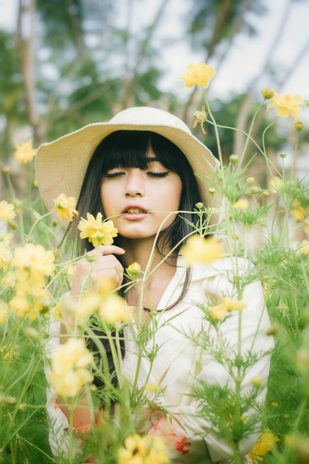 黄色い花畑に立っている茶色の日よけ帽をかぶった白い長袖シャツを着た女性
