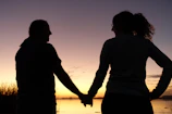 A couple holding hands under a soft pink sunset, symbolizing tender moments from our stories.